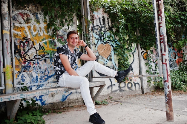 Lifestyle portrait of handsome man posing on the street of city with graffiti wall