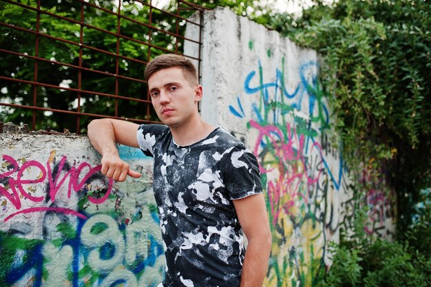 Lifestyle portrait of handsome man posing on the street of city with graffiti wall