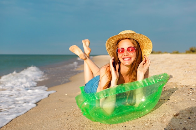 Il ritratto di stile di vita della donna bionda di bellezza felice giaceva nel materasso ad aria per prendere il sole in spiaggia, sorridere e godersi le vacanze estive