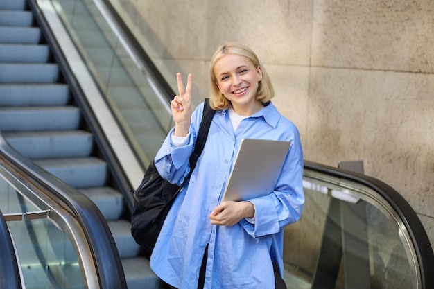 Lifestyle portrait of positive young woman female student with laptop and backpack showing peace