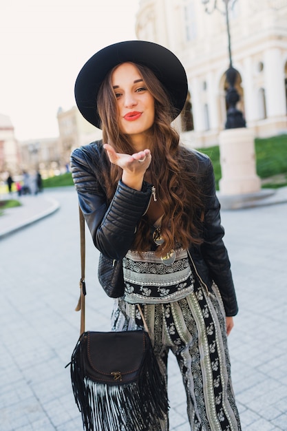 Lifestyle portrait of pretty cheerful woman send kiss, laughing, enjoying holidays in old European city. Street fashion look.  Stylish spring outfit.