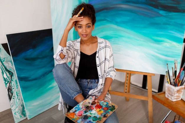 Портрет образа жизни молодого африканского студента сидя с художественным произведением изумительного абстрактного моря акриловой нарисованным рукой на студии.