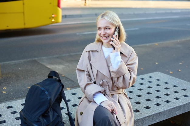 Free photo lifestyle portrait of young beautiful blond girl sitting on bench outside talking on mobile phone