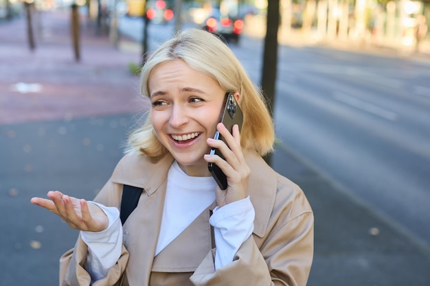 Free photo lifestyle portrait of young blond woman talking on mobile phone chatting with someone while walking