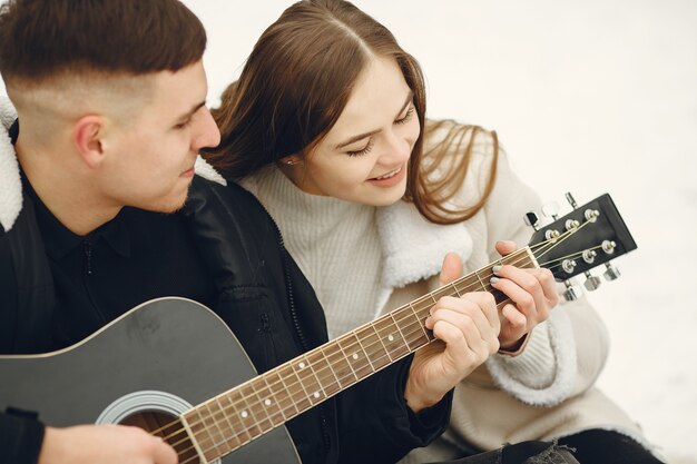 雪の森に座っているカップルのライフスタイルショット。冬休みを屋外で過ごす人々。カップルはギターを持っています。