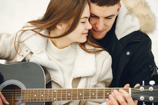 Lifestyle shot of couple sitting in snowy forest. People spending winter vacation outdoors. Couple wit a guitar.