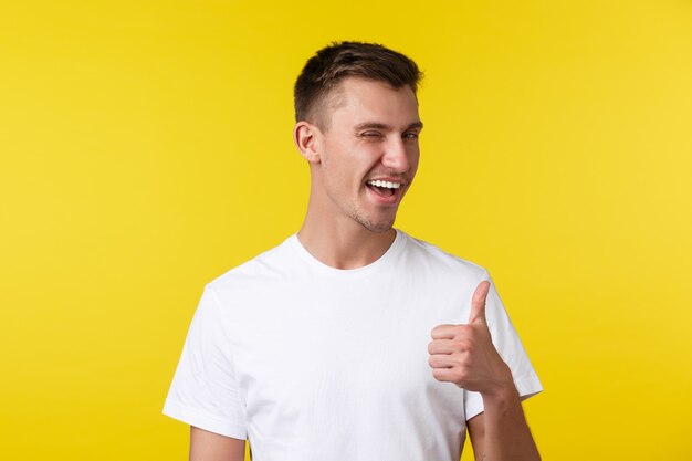 Lifestyle, summer and people emotions concept. Cheeky handsome happy man in white t-shirt, winking and thumbs-up, praising nice work, well done, congratulate on achievement.