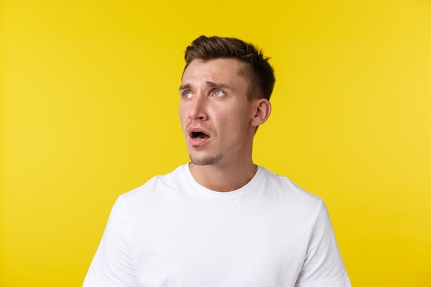 Lifestyle, summer and people emotions concept. Close-up portrait of disappointed sad and tired young man in white t-shirt, looking upper left corner, gasping and frowning upset over bad news.