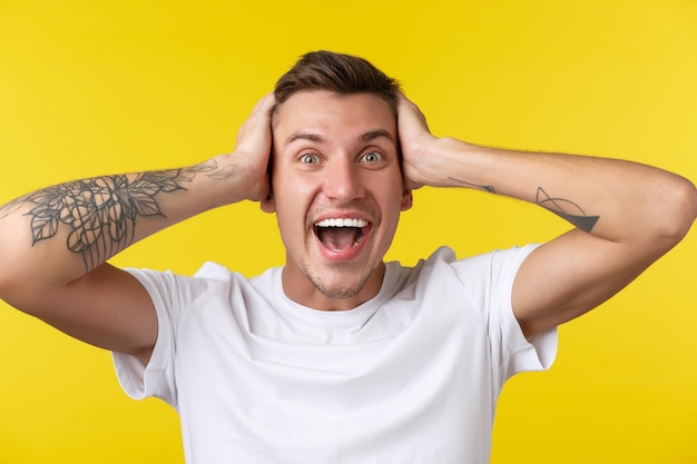 Lifestyle, summer and people emotions concept. close-up portrait of extremely happy rejoicing young man looking surprised, cant believe he won prize, hold hands on head in denial, yellow background