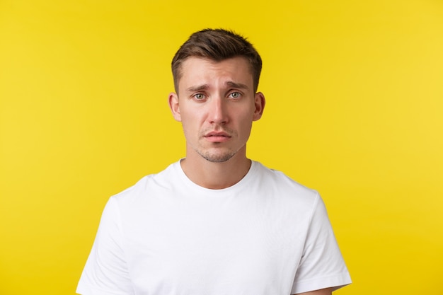 Lifestyle, summer and people emotions concept. Close-up portrait of miserable distressed young man looking gloomy and sad, feeling heartbroken or tired, frowning over yellow background