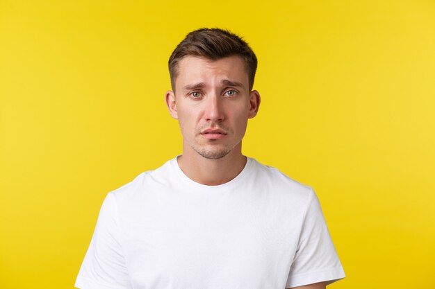 Lifestyle, summer and people emotions concept. Close-up portrait of miserable distressed young man looking gloomy and sad, feeling heartbroken or tired, frowning over yellow background