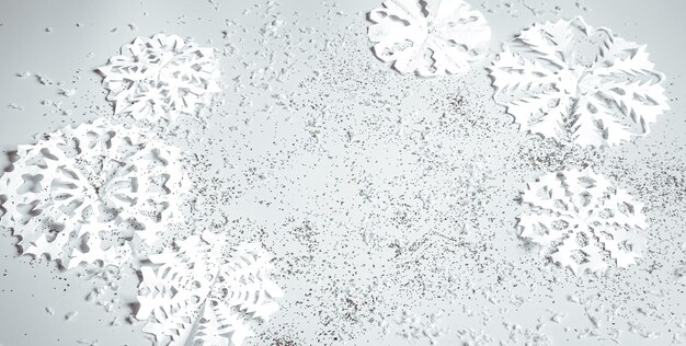 手でカットされた紙の雪片とスパンコールが平面にある明るい背景。クリスマスバナーのコンセプト。