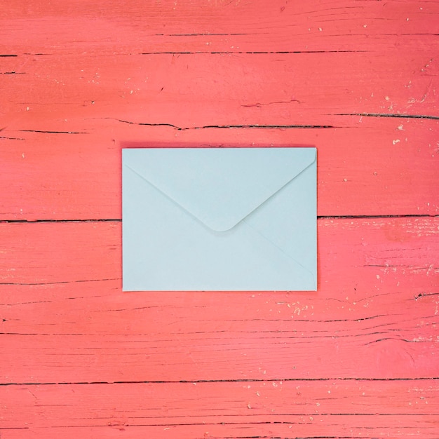 Голубой конверт на светло-розовом деревянном фоне