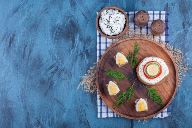 A light breakfast on wooden plate on pieces of fabric on blue. 