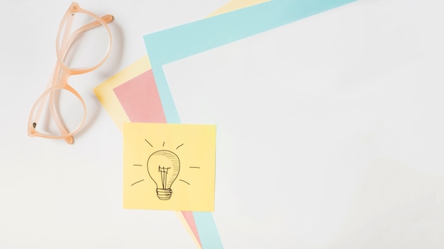 Free photo light bulb drawn on adhesive note over the card paper and eyeglasses on white background