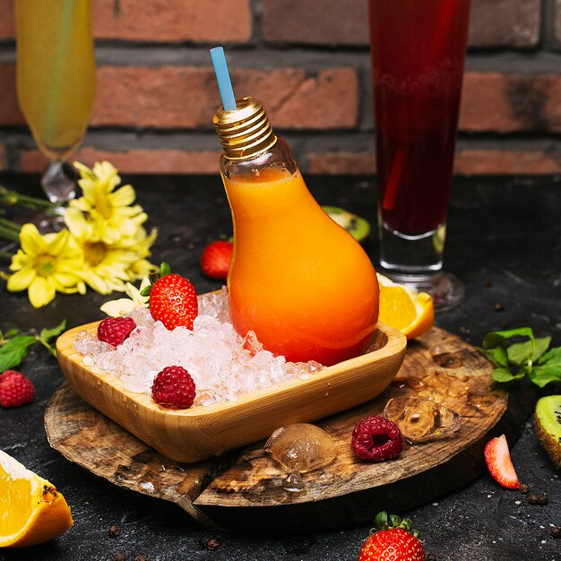 Light Bulb Glass Bottles with Fresh Orange Tropical Fruits Juice on plate with ices cubes and strawbesrries. Vacation Relaxation Detox Cleansing Wellness 