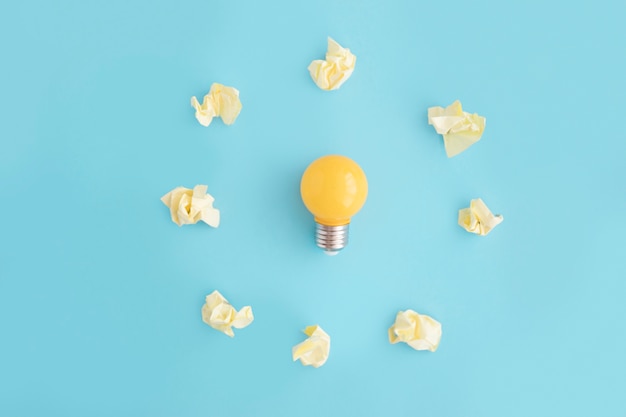 Light bulb surrounded with yellow crumpled paper on blue background