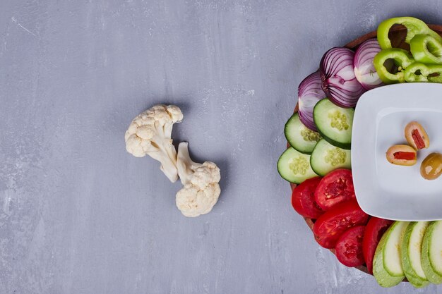 Light salad with vegetables and herbs in wooden platter, top view.