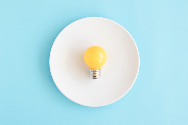 Светло-желтая лампочка на белом блюде на синем фоне