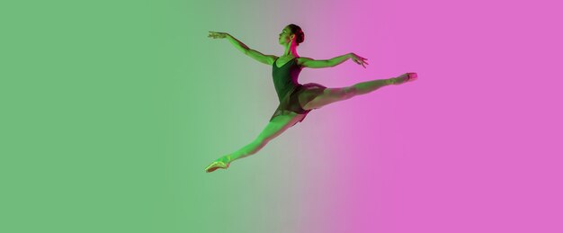 Свет. Молодой и изящный артист балета изолирован на градиентной розово-зеленой стене в неоне. Искусство, движение, действие, гибкость, концепция вдохновения. Гибкая балерина, прыжки в невесомости.