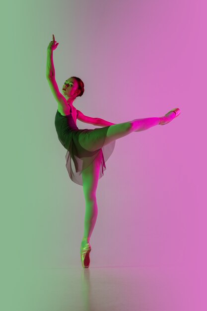 光。ネオンのグラデーションピンクグリーンの壁に分離された若くて優雅なバレエダンサー。アート、モーション、アクション、柔軟性、インスピレーションのコンセプト。柔軟なバレリーナ、無重力ジャンプ。