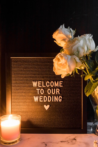 Зажженная свеча и розы возле черной рамки с приветствием к нашему свадебному сообщению