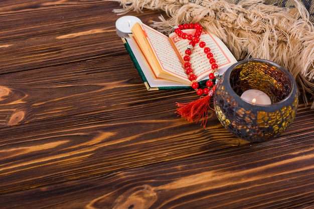 Lighted candle holder; kuran and red prayer beads on wooden desk