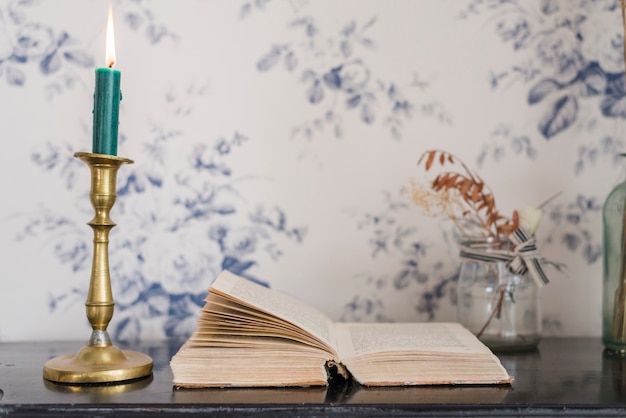 Зажженная свеча над подсвечником и открытая книга на столе на фоне обоев