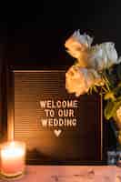 Free photo lighted candle and roses near the black frame with welcome to our wedding message