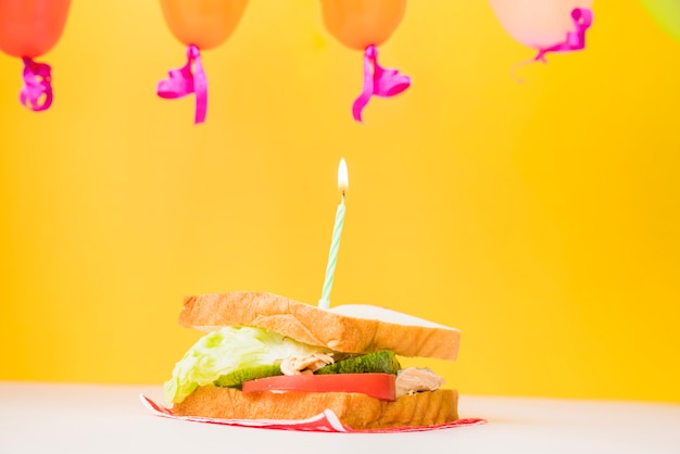 Зажженная свеча над сэндвичем на желтом фоне