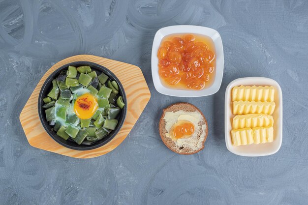 Lightly cooked bean pulses with scrambled egg, butterbrot, butter slices and white cherry jam on marble table.