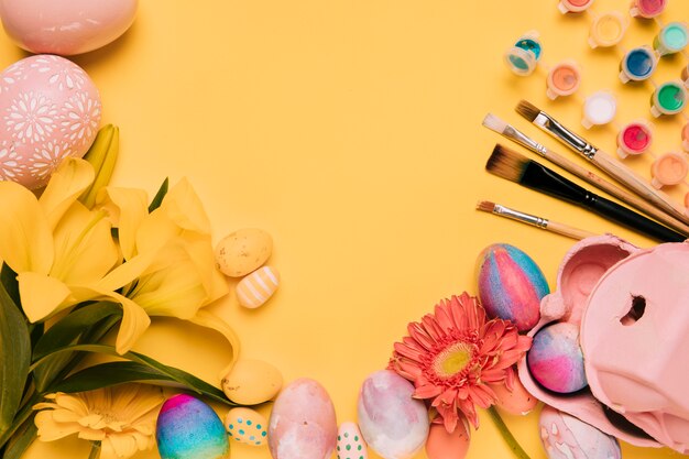 Lily; gerbera flower; paint brush; watercolor paint; with easter eggs on yellow background