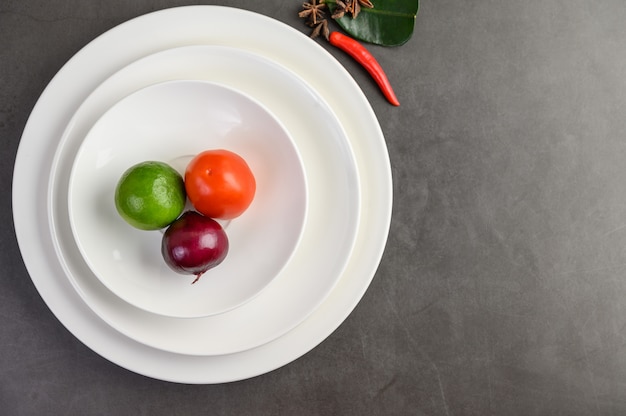 Лайм, красный лук и помидоры на белой тарелке.