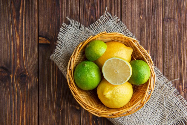 Limes in a wicker basket with lemons flat lay on wooden and piece of sack