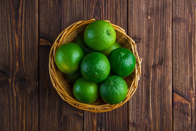 Limes in a wicker basket on a wooden table. flat lay.