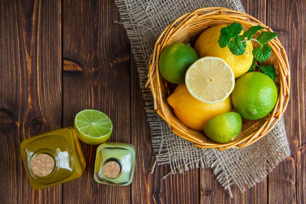 Limes with lemons, soft drinks, herbs in a wicker basket on wooden and piece of sack, flat lay.