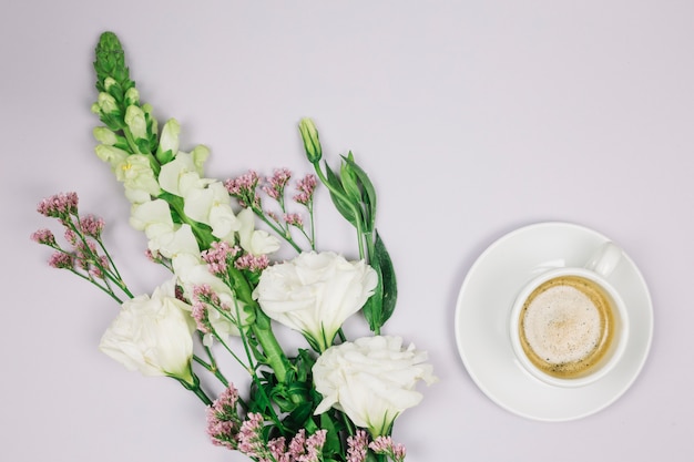 Limonium; eustoma and snapdragons flower bouquet near the coffee cup on white backdrop