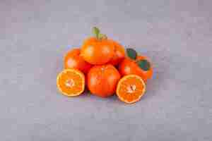Free photo line of sweet tangerine fruits with leaves placed on a stone .