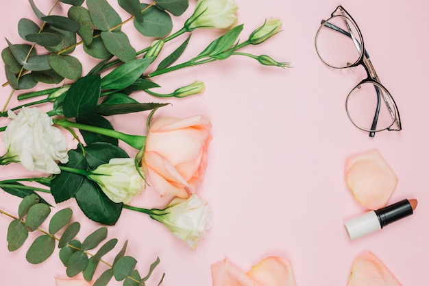Lipstick; eyeglasses and flower bouquet over pink background