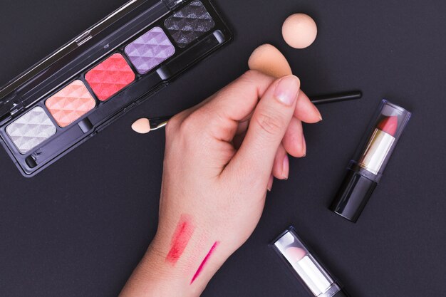 Lipstick marks on the female's hand with cosmetics products on black background