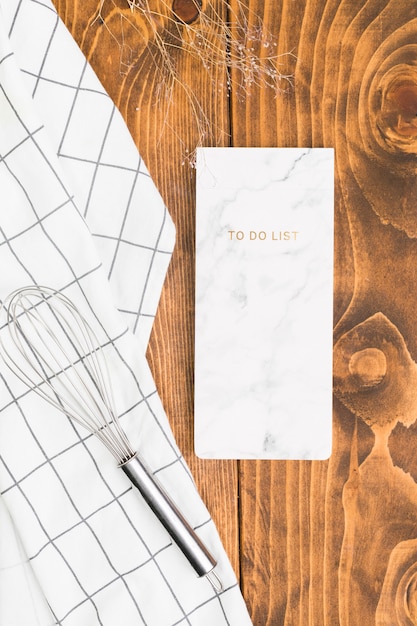 To do list notepad with whisk and checkered napkin over textured plank