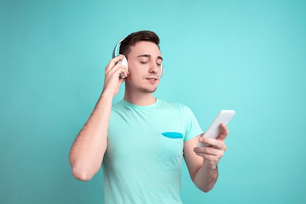 Listen to music. Caucasian young man's portrait isolated on blue studio wall