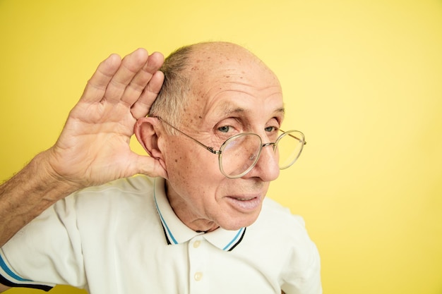 Listen to secrets. Caucasian senior man's portrait isolated on yellow studio background. Beautiful male emotional model. Concept of human emotions, facial expression, sales, wellbeing, ad. Copyspace.