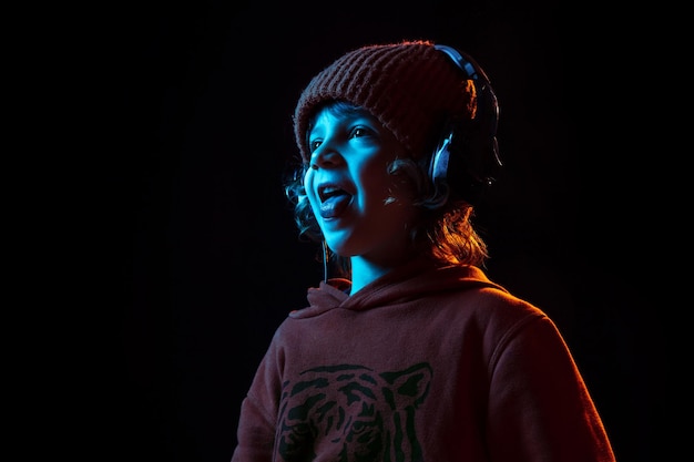 Listening to music and dancing. Caucasian boy's portrait on dark studio background in neon light. Beautiful curly model.