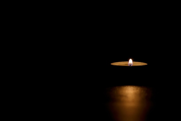 Free photo lit tin candle in the dark conveying memorial, death, hope or darkness