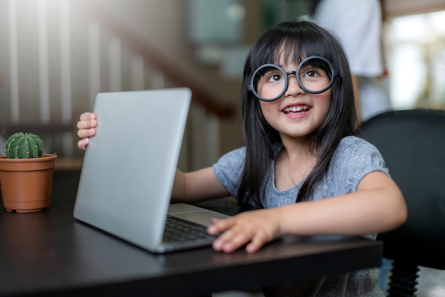 La piccola adorabile figlia indossa gli occhiali si diverte a giocare con il laptop fingendo di lavorare a casa sullo sfondo