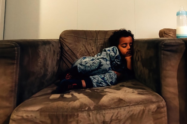 パジャマ​姿​の​小さな​アフリカ系​アメリカ人​の​子供​が​自宅​の​肘掛け​椅子​で​眠り​に​落ちました