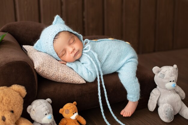 小さな赤ちゃん男の子かわいい新生児幼児のおもちゃに囲まれた青いかぎ針編みのピジャマの茶色のソファの上に敷設