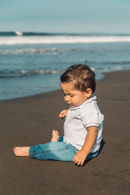 Маленький ребёнок сидя на песке пляжа