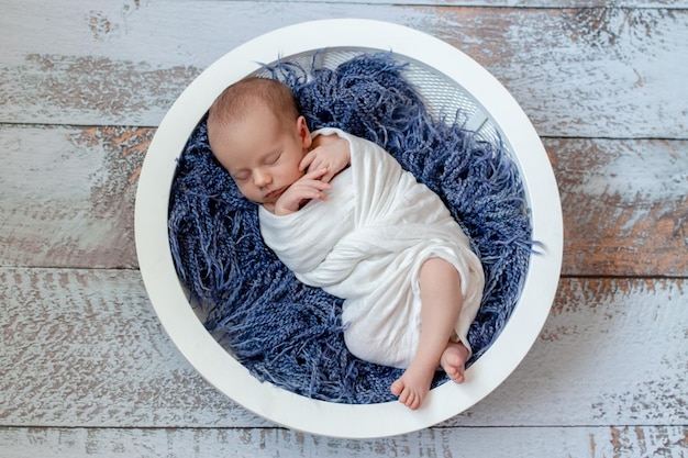 Foto gratuita piccolo neonato che dorme in un cestino sul pavimento di legno, colpo dello studio. neonato. 14 giorni